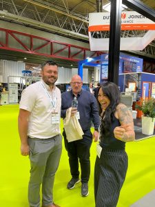 Three visitors smiling in the exhibition hall at a trade show